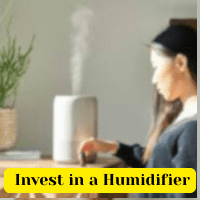 Winter Skincare Secrets 10 Ways to Keep Your Skin Smooth and Hydrated 6 A woman sitting beside a running humidifier with visible steam, promoting the message 'Invest in a Humidifier' highlighted in a yellow banner.
