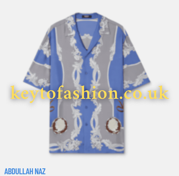 Why You’ll Love a Cameo Silk Shirt 4 A close-up of a blue and grey Versace Cameo Silk Shirt with short sleeves. The shirt features an ornate pattern with white floral-like designs and brown, circular elements. The background is plain white. "keytofashion.co.uk" is watermarked across the center of the image. "ABDULLAH NAZ" is written in blue text at the bottom left.
