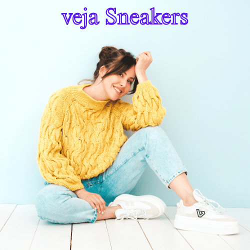 10 Remarkable Brands Like Idioma Every Style Enthusiast Will Fall in Love With in 2025 7 A smiling woman is sitting on a wooden floor in front of a light blue wall. She is wearing a yellow cable-knit sweater, light blue jeans, and white platform sneakers. Her hair is in a messy bun.