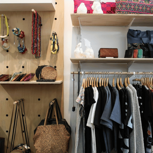 The Art of Accessory Design and How Small Details Define Big Fashion Statements 2 A stylish fashion boutique interior showcasing clothing on racks and accessory items like handbags, purses, and necklaces neatly displayed on wooden shelves.